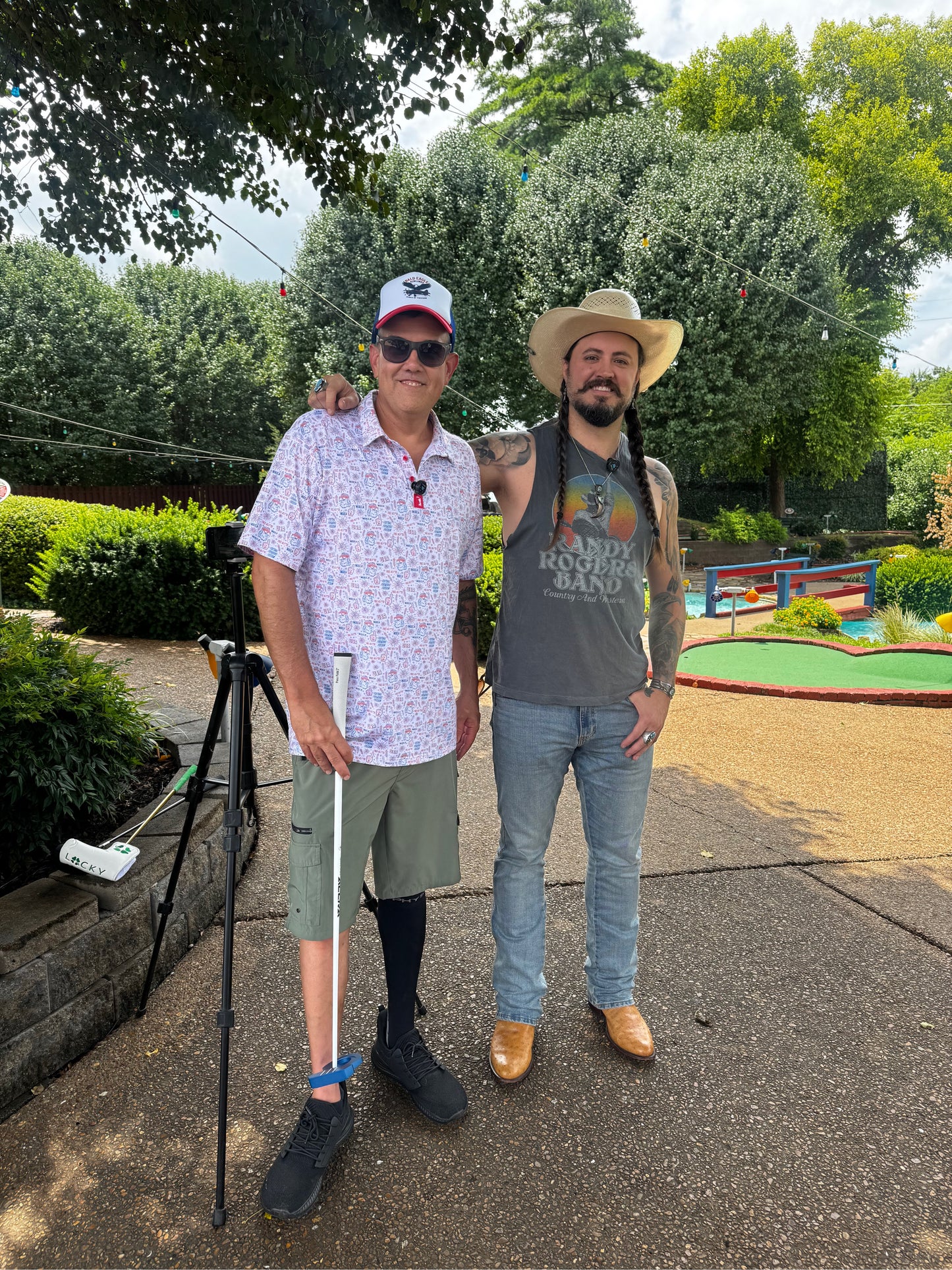 Two men standing outdoors with trees and a mini golf course in the background