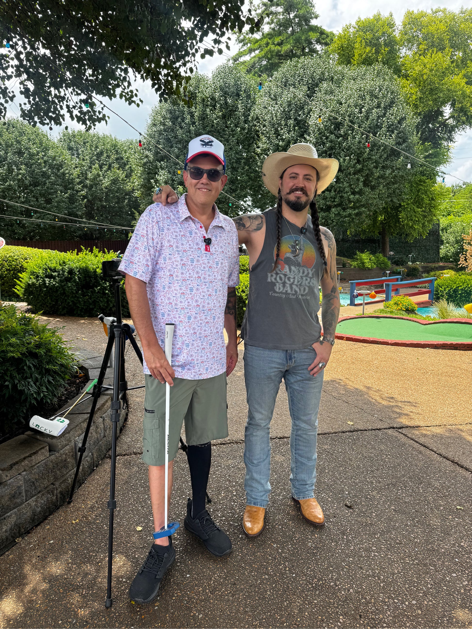 Two men standing outdoors with trees and a mini golf course in the background